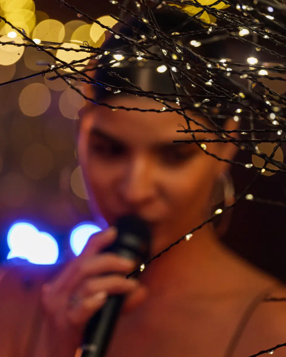 A singer close to the microphone, string lights out of focus around her